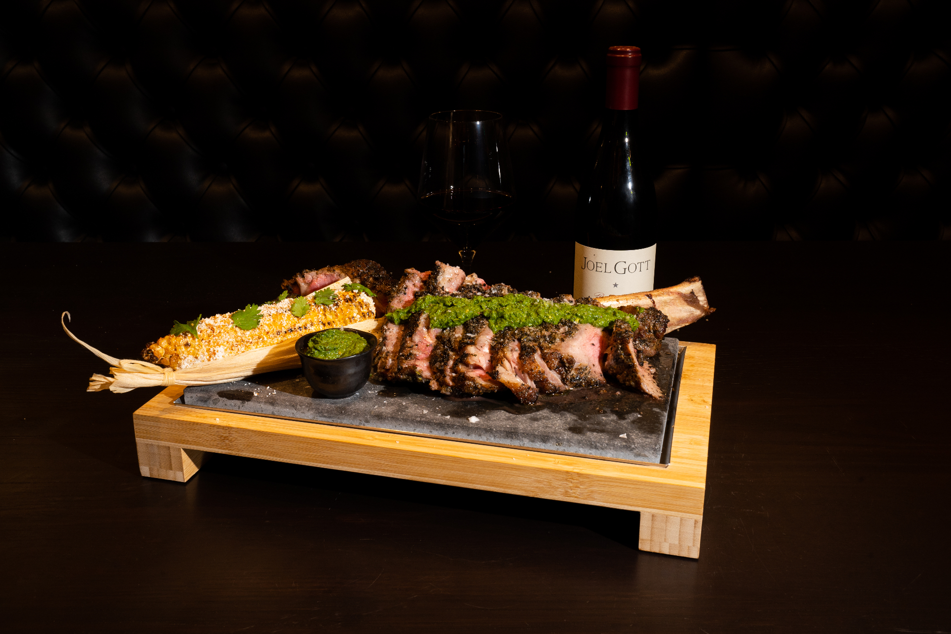Tomahawk steak presentation with elote, chimichurri, and red wine